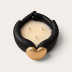 Vela artesanal THE IBIZA CANDLES Black Tuxedo con forma de manos negras sosteniendo un corazón dorado y tres mechas.