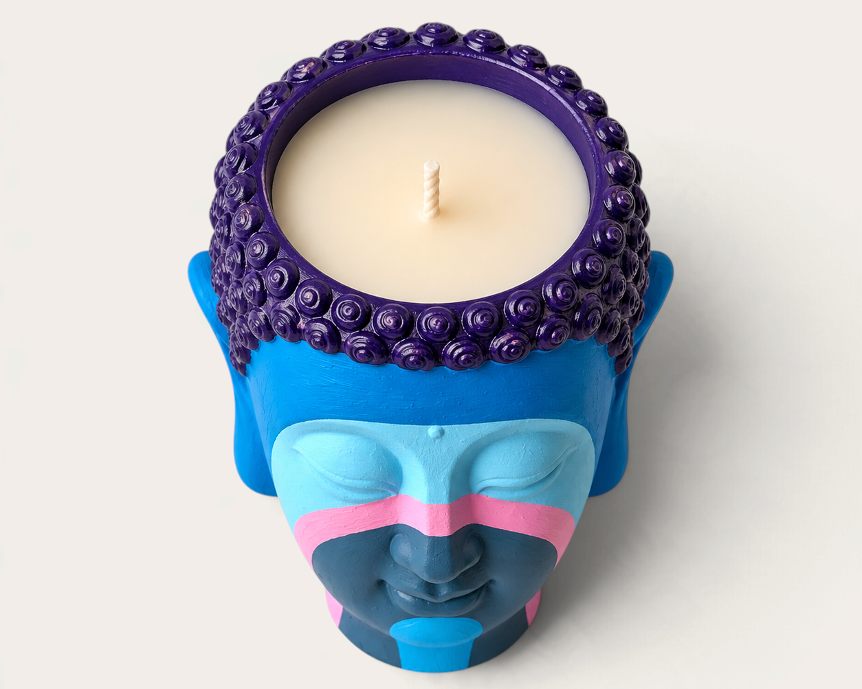 Vela artesanal THE IBIZA CANDLES con forma de cabeza de Buda pintada a mano en tonos azul, violeta y rosa.