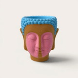 Vela artesanal THE IBIZA CANDLES modelo Indian con forma de cabeza de Buda pintada en tonos azul, rosa y terracota.