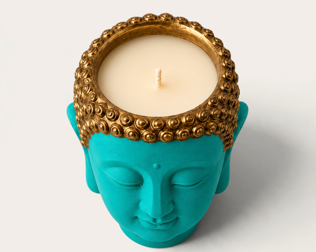 Vela artesanal THE IBIZA CANDLES con forma de cabeza de Buda en color turquesa y detalles dorados en el cabello.