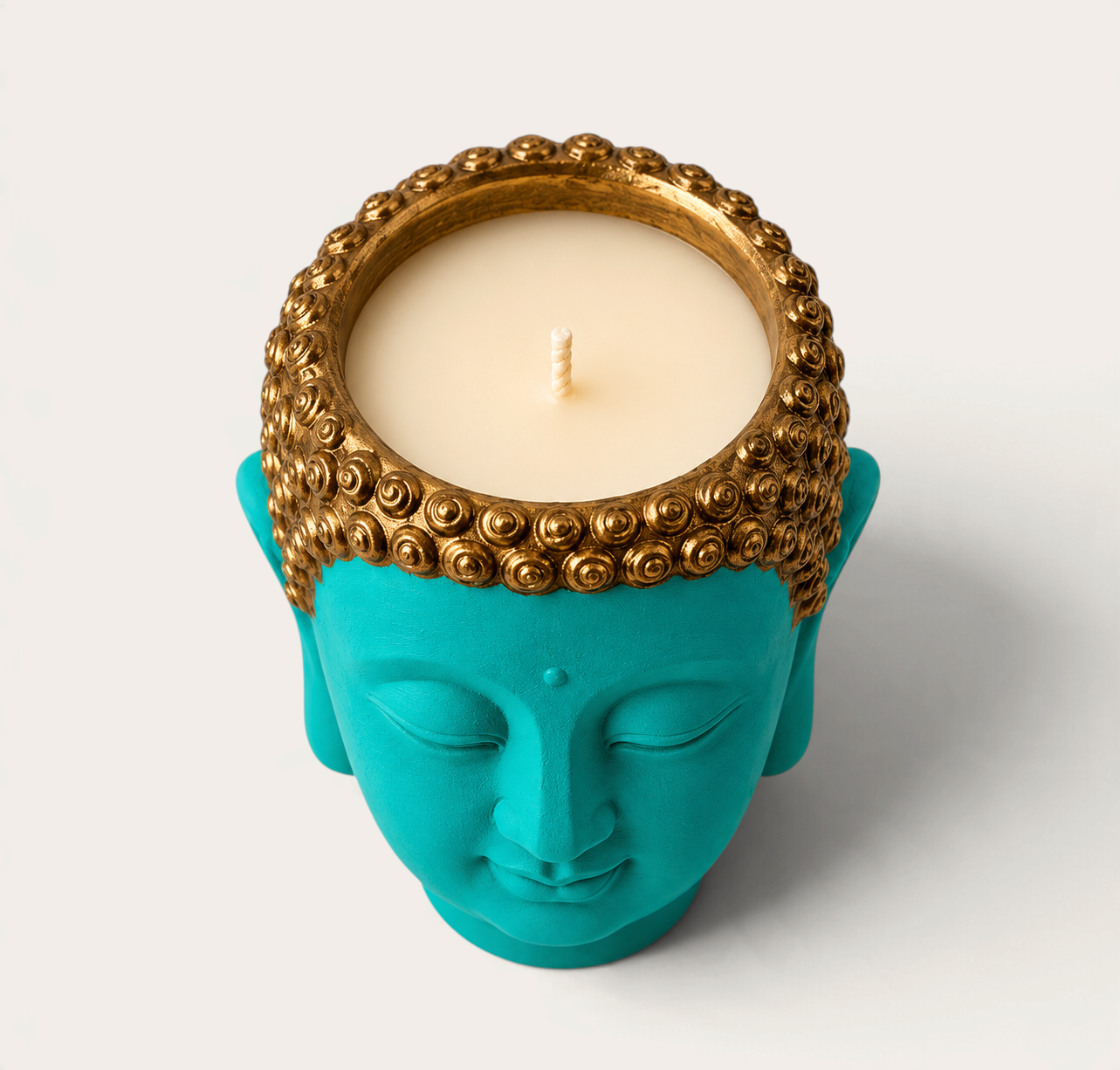 Vela artesanal THE IBIZA CANDLES con forma de cabeza de Buda en color turquesa y detalles dorados en el cabello.