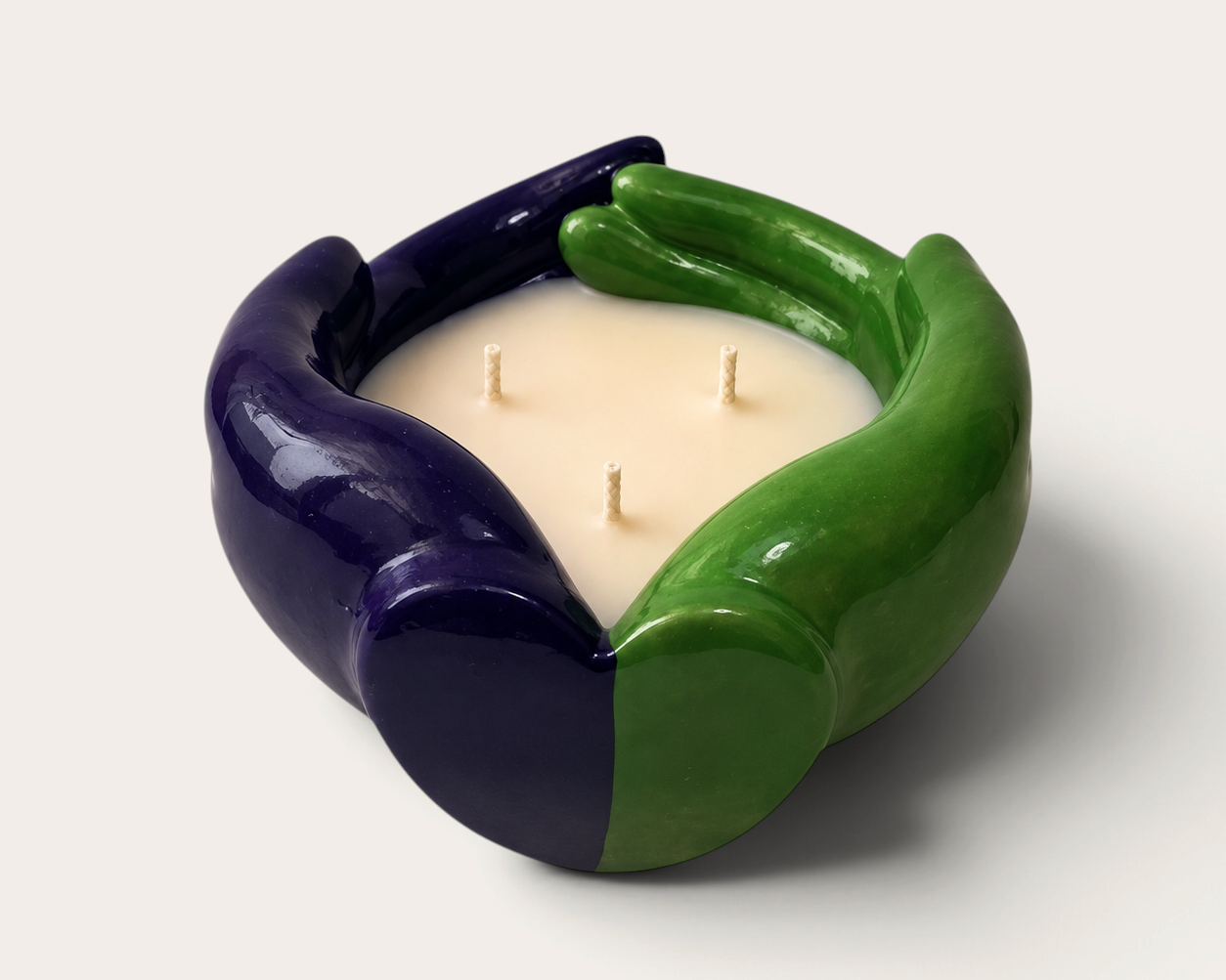Vela artesanal THE IBIZA CANDLES con forma de manos entrelazadas en colores verde y morado, diseño escultórico.