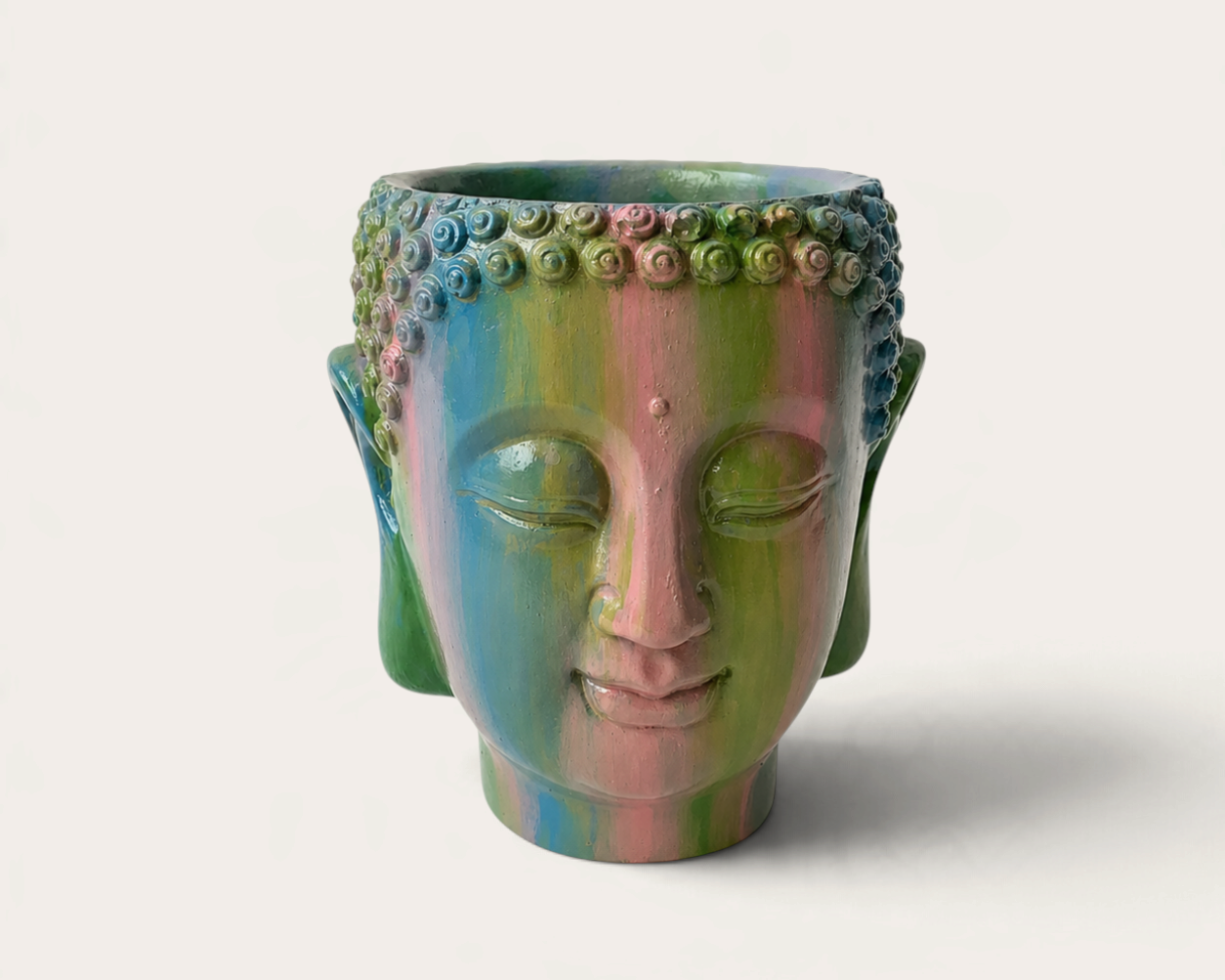 Vela escultórica THE IBIZA CANDLES con forma de cabeza de Buda pintada a mano en tonos arcoíris sobre fondo neutro.