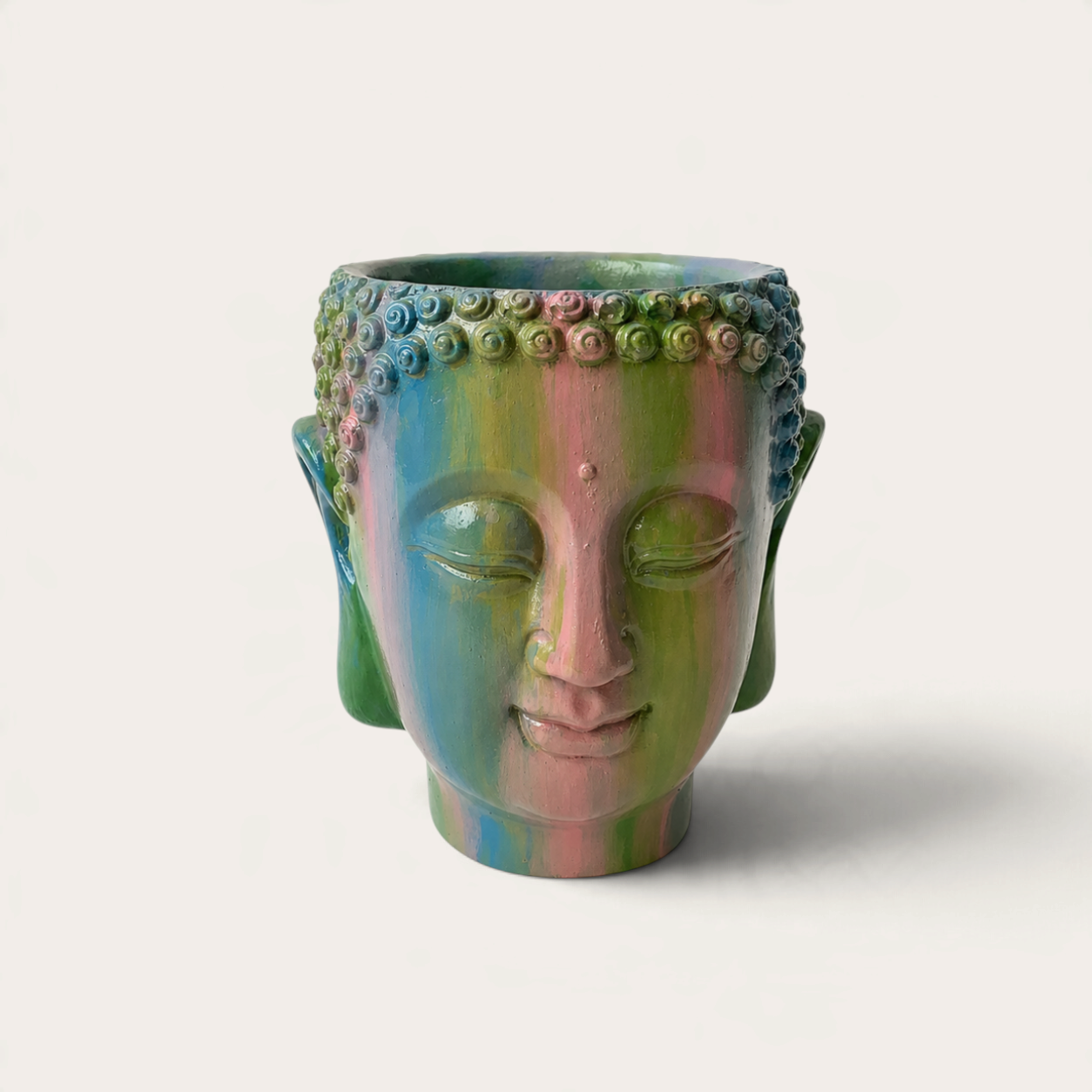 Vela escultórica THE IBIZA CANDLES con forma de cabeza de Buda pintada a mano en tonos arcoíris sobre fondo neutro.