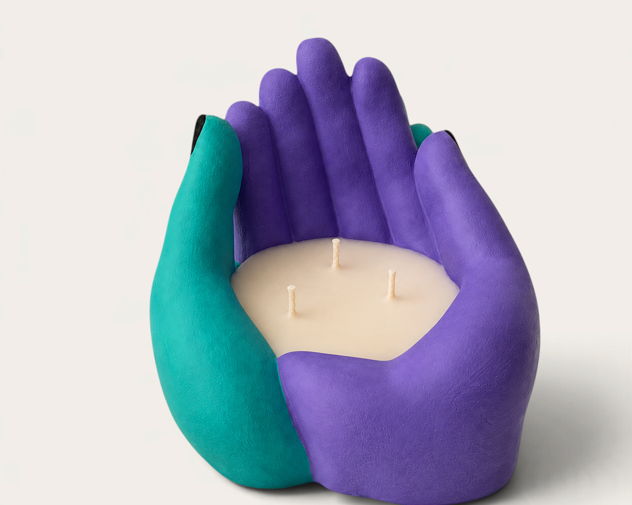 Vela artesanal THE IBIZA CANDLES con forma de manos entrelazadas en color morado y turquesa, diseño escultórico.