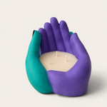 Vela artesanal THE IBIZA CANDLES con forma de manos entrelazadas en color morado y turquesa, diseño escultórico.