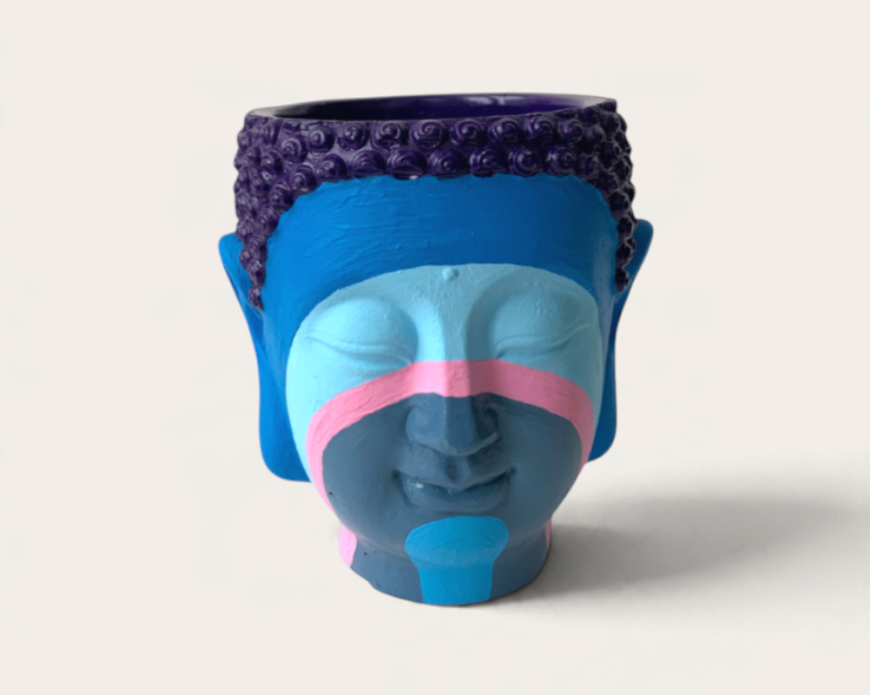Vela artesanal THE IBIZA CANDLES con forma de cabeza de Buda pintada a mano en tonos azules, morados y rosas.