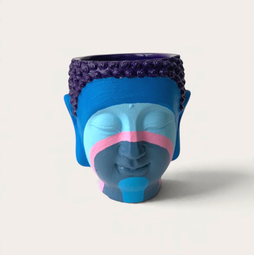 Vela artesanal THE IBIZA CANDLES con forma de cabeza de Buda pintada a mano en tonos azules, morados y rosas.